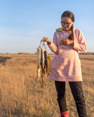 Yakut young joyful girl angler hard holds in his hands a lot of fish caught pike hanging on Fish Stringer in the field.
