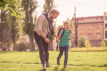 two people, young man and his son or younger brother, running in the grass field in the city. Holding hands together. Excited and happy, full lenght portrait.