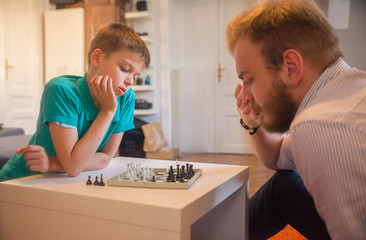 Young man and his son playing chess. Both are thinking about their next moves.