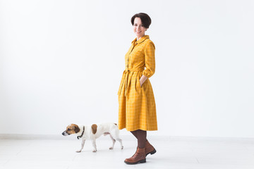 Cheerful young woman posing in a yellow dress with her beloved dog Jack Russell Terrier standing on a white background. The concept of casual wear and pets