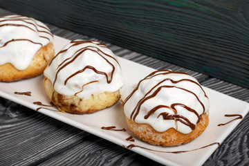 Cinnabons in white glaze, decorated with chocolate. Lie on a plate. Against the background of brushed pine boards.