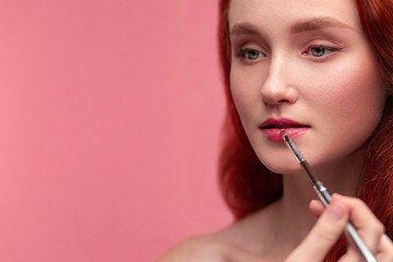 Makeup artist applies lipstick. Hand of make-up master, painting lips of young redhead girl....