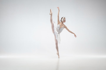 Fototapeta na wymiar Moving. Young graceful classic ballerina dancing on white studio background. Woman in tender clothes like a white swan. The grace, artist, movement, action and motion concept. Looks weightless.