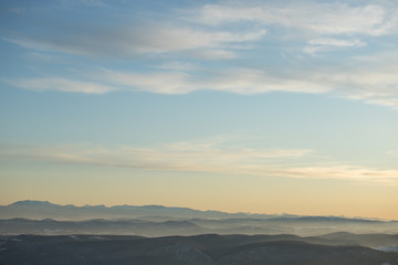 Beautiful view of the mountain range partially covered with snow just before sunset. Partly orange sunset sky
