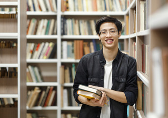 Smiling korean guy holding textbooks at library