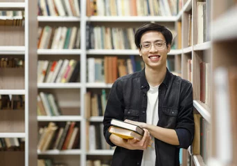 Fotobehang Smiling korean guy holding textbooks at library © Prostock-studio