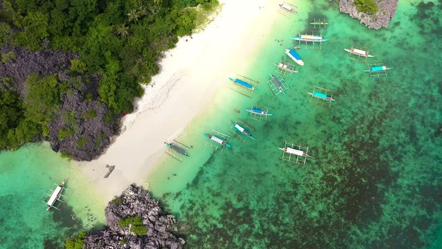 Tropical landscape:Matukad Island with beautiful beach and tourists by turquoise water view from above. Caramoan Islands, Philippines.  Boats and tourists on the beach.