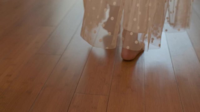 A young woman walks barefoot on the parquet in a sunny room. Slow motion.
