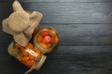Canned tomatoes in glass jars on dark wooden board. Space for text. View from above.