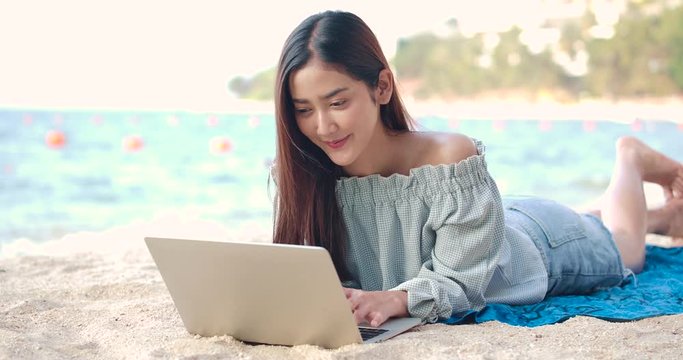 Woman freelancer works on the beach. Young asian female working with computer laptop on the tropical island beach with happy emotion. Technology for wherever concept.