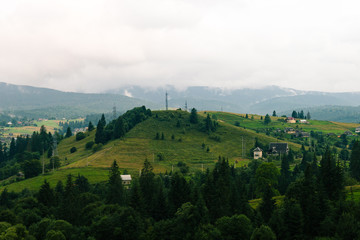 Ukrainian village in the Carpathian mountains in cloudy .day. Country side view of vertex in the middle of summer in nasty day. Rural landscape with forest, hills, authentic houses without people.