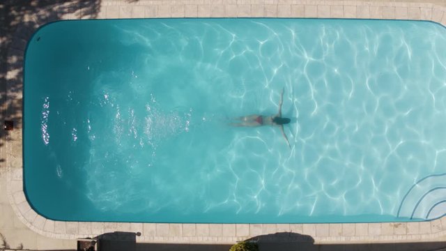 Aerial view of woman with swimsuit swimming on a blue water pool. Top view of woman dives in the pool and swims using the breaststroke.