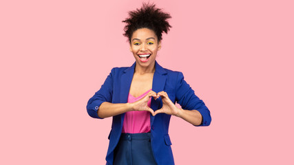Smiling afro girl showing heart gesture at pink studio