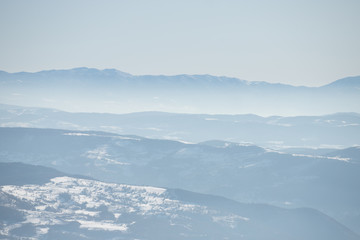 Beautiful view of the mountain range partially covered by fog and snow with clear blue sky.