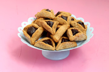 Homemade hamantaschen cookies in a serving plate on pink background with copy spce. Purim celebration concept (jewish carnaval holiday).