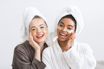 Joyful young women in bathrobes applying eye patches