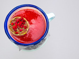 red smoothie from berries, with goji, orange slice in blue mug