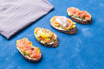 Sandwiches with smoked salmon, eggs, sauce and avocado on blue background. Concept of breakfast and healthy nutrition.