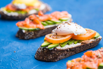 Sandwiches with smoked salmon, eggs, sauce and avocado on blue background. Concept of breakfast and healthy nutrition.