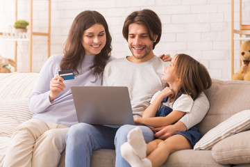 Happy family sitting on couch with laptop and credit card