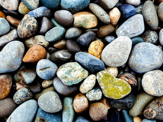 Background of horizontal orientation from multicolored pebbles: blue, grey, orange, brown, one green pebbles similar to heart, located in the right lower part of the frame