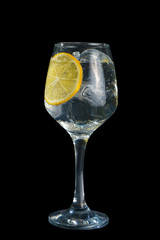 Transparent cocktail, refreshing water in a tall glass with ice cubes and a round slice of lemon, side view, isolated black background. Drink for the menu restaurant, bar, cafe