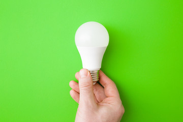 Young man hand holding led light bulb on bright green table background. Closeup. Energy saving....