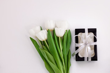 White tulip flowers and black gift box on light background flat lay. Place for text 8 March Happy Womens Mothers Day.Flower Bouquet with silver ribbon, greeting card.Copy space website banner top view