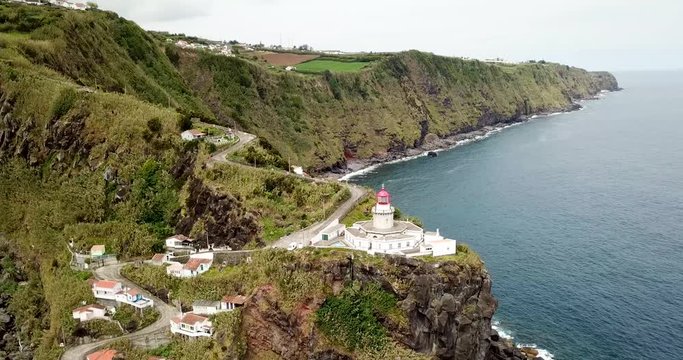 Azores Sao Miguel Lighthouse Arnel at the cliff close to ocean with a little village filmed by drone / aerial
