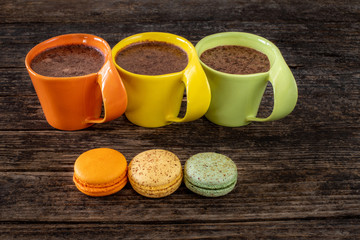 Many colorful macaroons on the table with coffee and hot chocolate