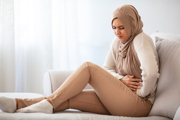Abdominal pain. Troubled muslim woman in hijab touching stomach, suffering from food poisoning or period cramps with free space. Sick Muslim Woman In Hijab Having Acute Abdominal Or Menstrual Pain