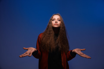 Portrait of a young beautiful serious girl on a trendy classic blue background. The girl spread her arms to the sides in surprise.