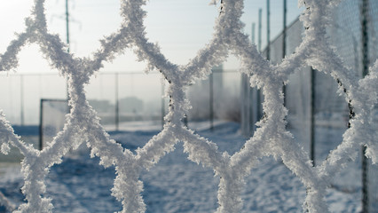 Frozen fence made of metal mesh covered with snowy hoarfrost, winter day