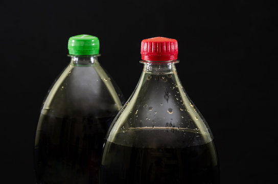 two bottles of carbonated drink on a black background. Close-up. Top of bottles with cap.