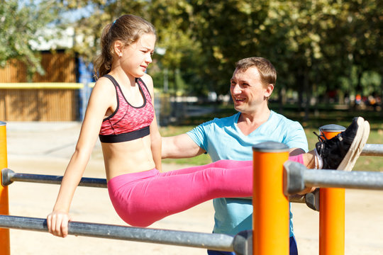 Girl with father doing l-sit on parallel bars