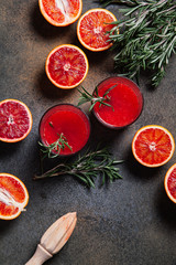 Blood orange juice with rosemary sprigs in a glass, sliced Sicilian blood oranges on a rustic background.