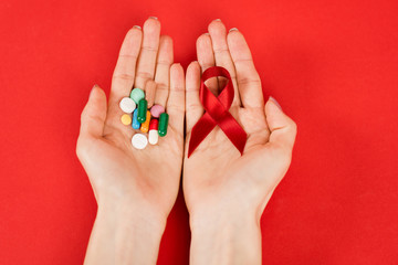 top view of woman holding red ribbon as hiv awareness and pills on red