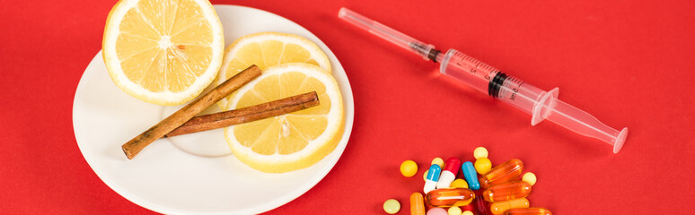 panoramic shot of syringe near sliced lemons, cinnamon sticks and pills on red