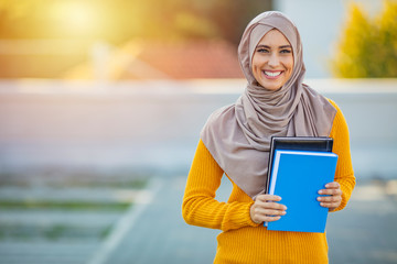 Muslim girl, a college student, holding her workbooks at student campus. Muslim woman with...
