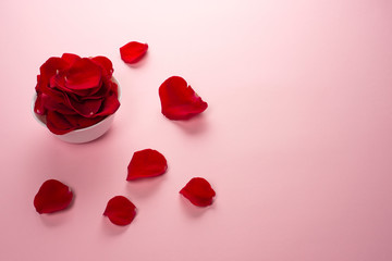 Beautiful red Rose petals in a white bowl and petals on the table on tender pink background.