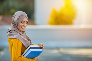 Beautiful female middle eastern college student. Pretty muslim female student with hijab is carrying books. Muslim women holding her workbooks. Portrait Of Female University Student