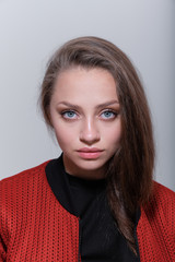 A close-up portrait of a young beautiful serious girl with blue eyes and brown hair in a black...