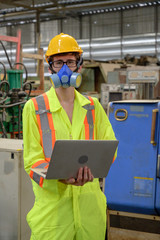 Caucasian male with protective mask with laptop working in factory area.