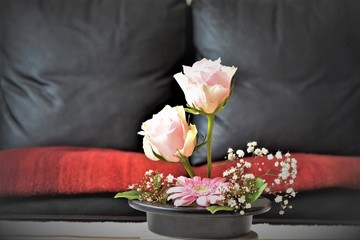 Pink rose ikebana flower arrangement in front of a black couch
