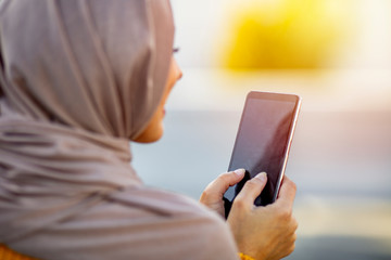 Woman wearing hijab browsing internet on mobile phone outdoors. Portrait of a modern arabian girl using mobile phone on the street. Close up of beautiful woman wearing hijab smiling while texting