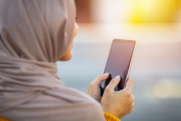 Female in her 20s wearing hijab texting on cellphone on urban street. Young woman wearing hijab head scarf in city texting cell phone. Portrait of happy muslim woman using mobile phone