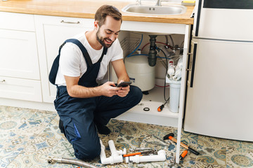 Man plumber work in uniform indoors using mobile phone. - obrazy, fototapety, plakaty