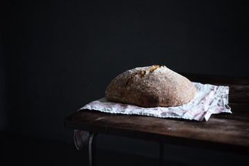 Appetitliches Bio Sauerteig Brot auf einem Leintuch auf  Holztisch vor dunkelem Hintergrund
