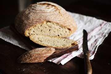 Appetitliches Bio Sauerteig Brot mit Brot Scheiben auf einem Holzbrett mit Leintuch vor einem dunkelen Hintergrund