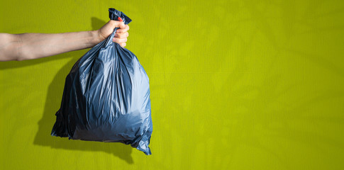 hand holding the  dark blue trash bag, concept of cleaning earth planet,isolated against the colored wall, simple concept